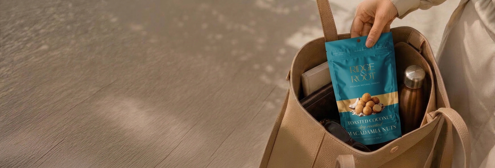 A hand holding a Toasted Coconut Ridge & Root macadamia pouch over a canvas tote bag