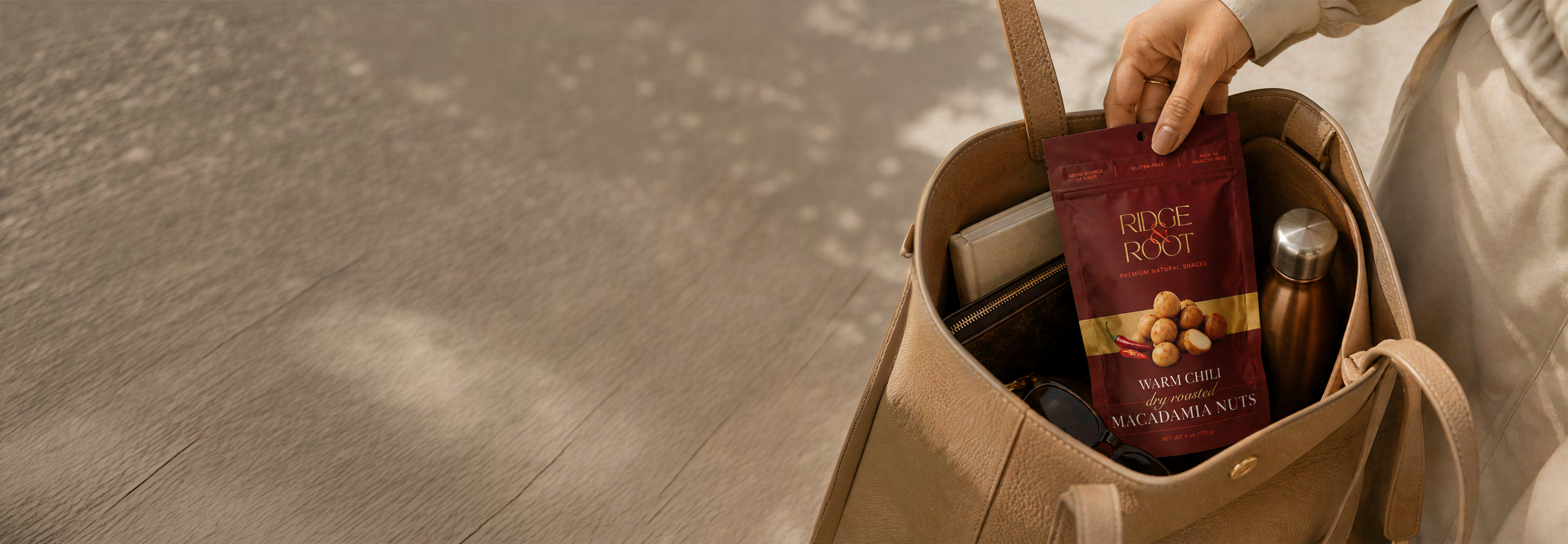 A hand holding a Warm Chili Ridge & Root macadamia pouch over a canvas tote bag